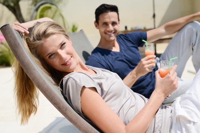 Mit einem coolen Drink lässt es sich aushalten wenn man dann auch noch eine Terrassenliege hat Junges Paar mit Getränken entspannt auf Terassenliegen