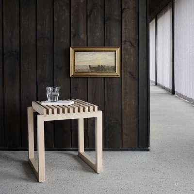 Hygge – so wird Wohnen zum Wohlfühlen 10 Perfekt für die Wasserkaraffe: Skagerak Cutter Hocker aus hellem Holz vor einer dunklen Wand.