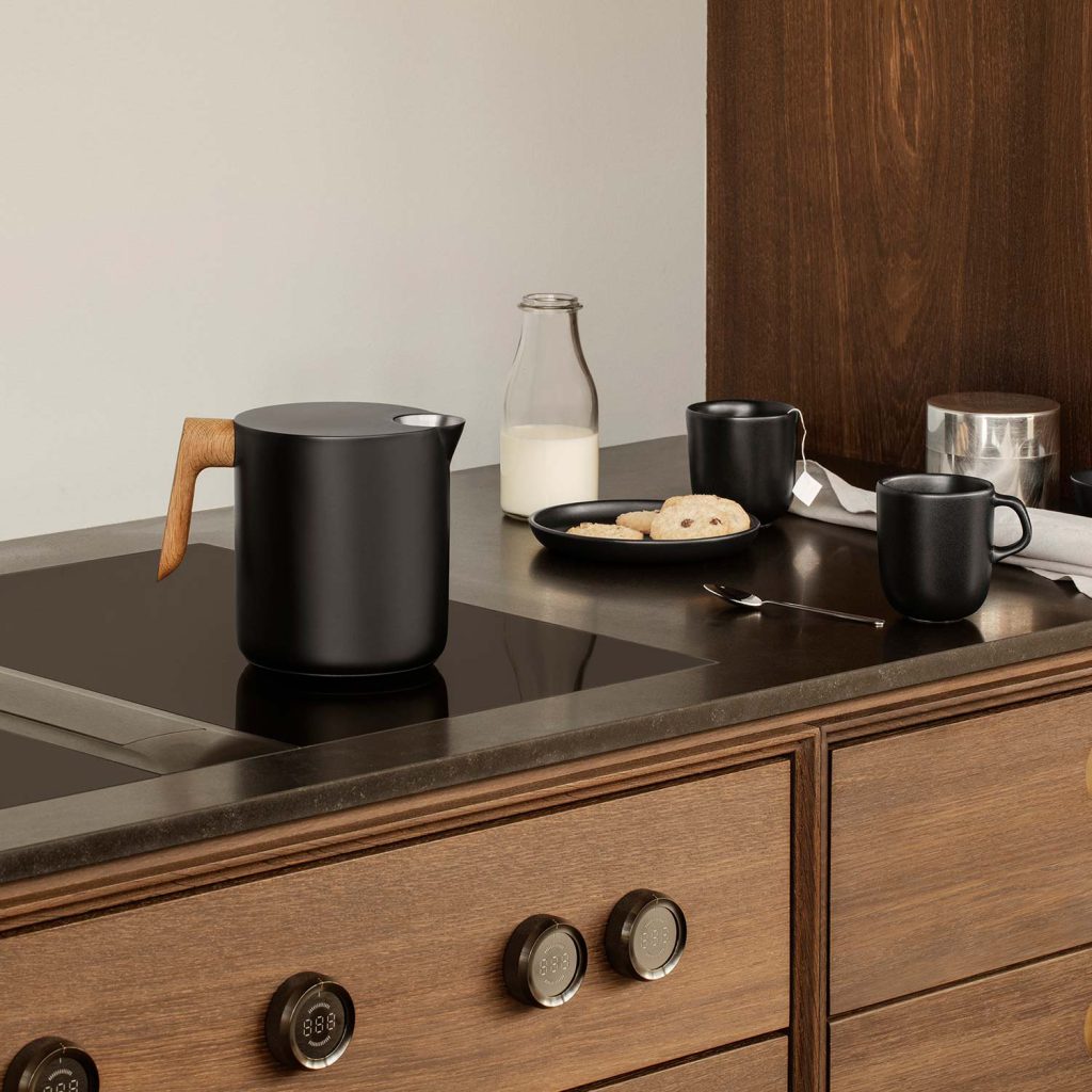 Hygge – so wird Wohnen zum Wohlfühlen 7 Der elegante Eva Solo Nordic Kitchen Wasserkessel in Schwarz mit Holzgriff auf einem Induktionsherd.